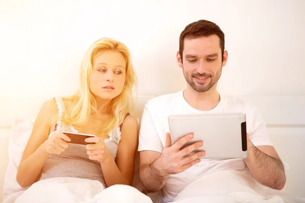 Joven pareja atractiva usando móvil y tableta en la cama —  Fotos de Stock