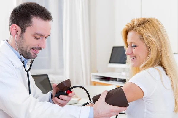 Giovane medico attraente che controlla la pressione sanguigna del paziente — Foto Stock