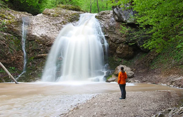 Chica se encuentra cerca de la hermosa cascada ancha y mirando — Foto de Stock