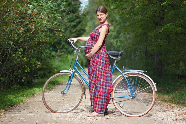 Chica embarazada con bicicleta en un camino forestal, vista lateral Fotos de stock libres de derechos