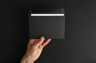 Beyaz erkek eli siyah arkaplanda beyaz harf olan boş bir zarf tutuyor, kopyalama alanı olan bir model.