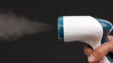 El ele tutuşun, portatif elbise buharlı vapurla siyah arka plandaki kıyafetler için çalışın.