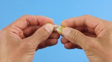 Eller sarı şeker lolipoplarından birini şeffaf bir ambalajdan, mavi arka plandan, sağlıksız şeker şekerlerinden çıkarır.