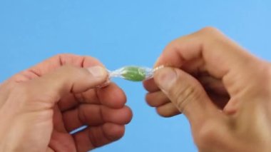 Eller, şeffaf bir ambalaj kağıdından yeşil şeker lolipopu çıkarır. Mavi arka plan, stresi şekerle yok etme girişimi.