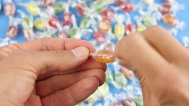 Hände Entfalten Ein Orangefarbenes Bonbon Aus Einer Transparenten Verpackung Auf — Stockvideo