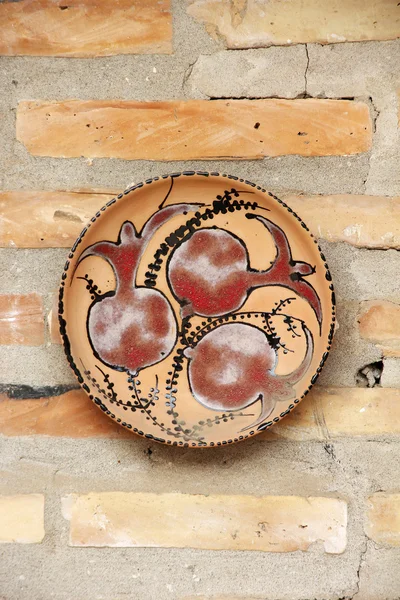 Керамическая плита с покрашенным гранатом на кирпичной стене — стоковое фото