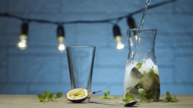 Sürahiye nane ve tutkulu meyve suyu ile köpüklü su dök. Mavi arka planda bulanık lambalar. Kamerayı kaydır ya da hareket ettir, dolly shot
