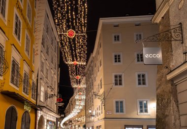 SALZBURG, AUSTRIA - 23 Aralık 2024: Meşhur tarihi Getreidegasse sokağı, Noel zamanı ışık dekorasyonlu alışveriş caddesi