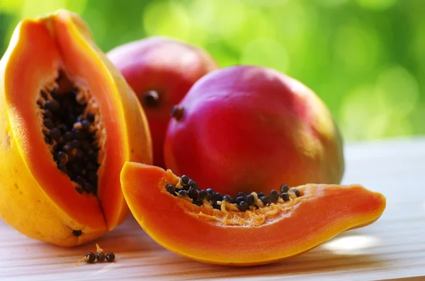 Papaya en rodajas y dos mangos en la mesa . — Foto de Stock