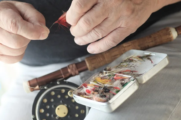 Fly fisherman with gear holds an artificial fly — Stock Photo, Image