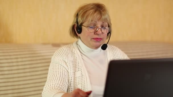 Женщина в наушниках с микрофоном разговаривает с клиентом через компьютер — стоковое видео