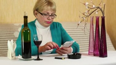 Kadın masada oturur, kırmızı şarap içiyor ve akıllı telefon kullanır