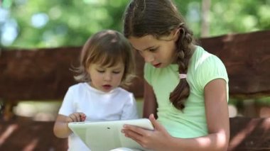 Tablet bilgisayar iki kızla salıncak bankta oturur