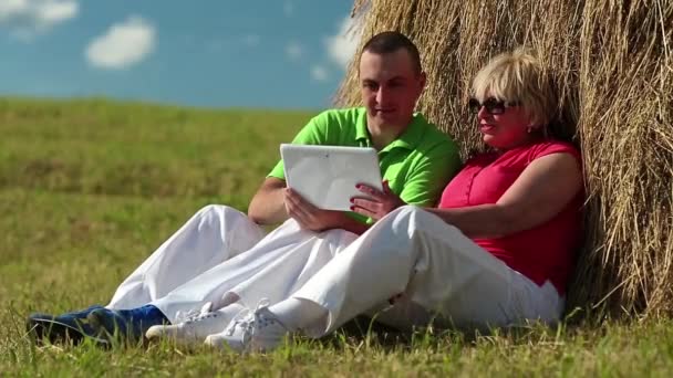 Man and woman with Tablet-PC sits near a haystack — Stock Video