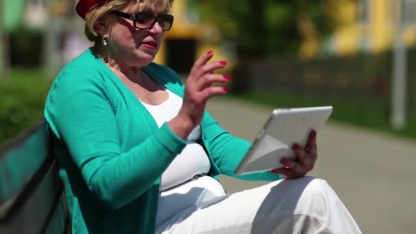 Mujer se sienta en el banco y se comunica a través de la tableta — Vídeos de Stock