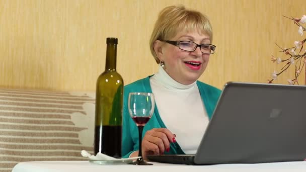 Kvinna med en flaska vin sitter vid ett bord och kommunicerar via laptop — Stockvideo
