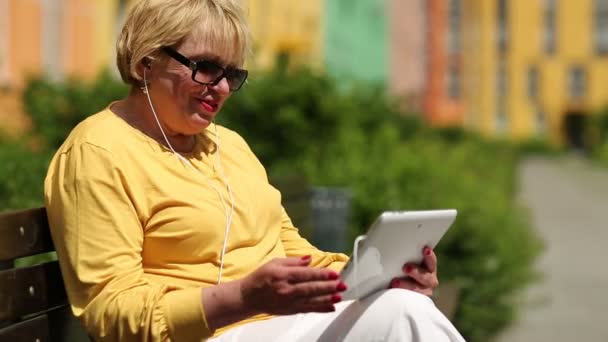 Mulher senta-se no banco e se comunica via tablet PC — Vídeo de Stock