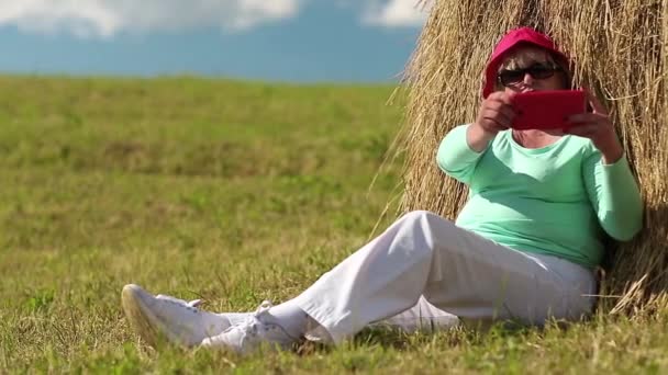 Femme assise sur l'herbe verte près de la botte de foin et fait des photos sur smartphone — Video