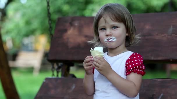 Little girl sits on the bench and eats ice cream — Stock Video