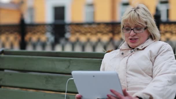 Femme avec tablette PC s'assoit sur le banc et parle sur Skype — Video