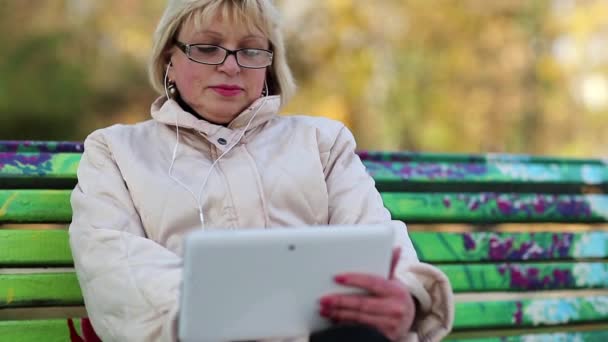 La mujer se sienta en el banco y usa una tableta. Mujer con Tablet PC — Vídeos de Stock