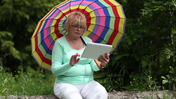 Mujer se sienta en un árbol caído y utiliza tableta PC — Vídeo de stock