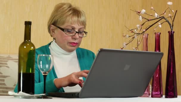 Kvinna med en flaska vin sitter vid ett bord och skriver text på laptop — Stockvideo