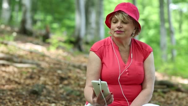 Kvinna i röd t-shirt och röd mössa i skogen lyssnar på musik — Stockvideo