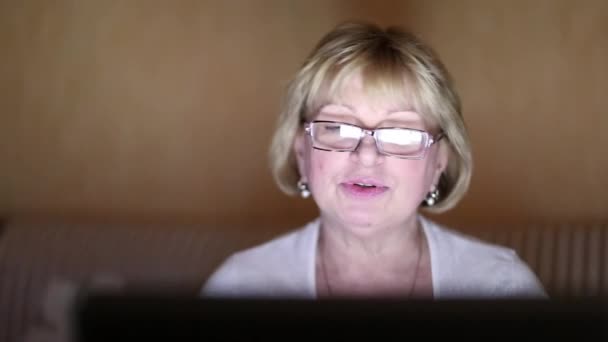 Vrouw zit op de Bank in een donkere kamer en communiceert via laptop — Stockvideo