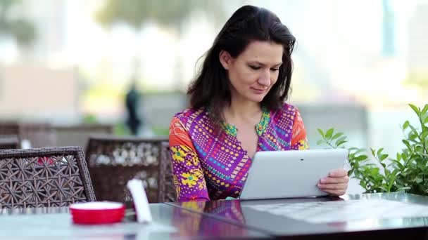 Mulher com computador tablet branco senta-se a uma mesa em um café — Vídeo de Stock