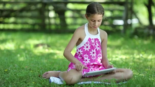 Jolie fille avec tablette informatique est assis sur l'herbe — Video