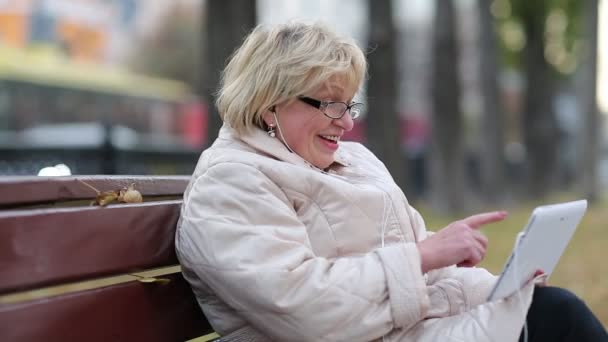 Senior woman sits on the bench near the road and communicates via tablet PC — Stock Video