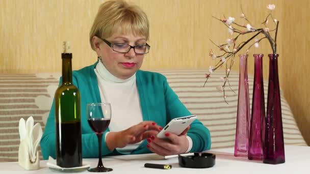 Mulher senta-se à mesa, bebe vinho tinto e fala no smartphone — Vídeo de Stock