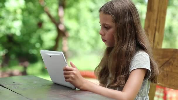 Mooi meisje met witte tabletcomputer zit aan de tafel — Stockvideo