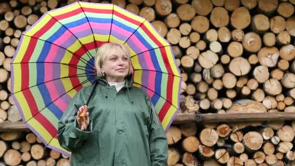 Vrouw in groene regenjas staat in de buurt van timmerhout en glimlachen — Stockvideo