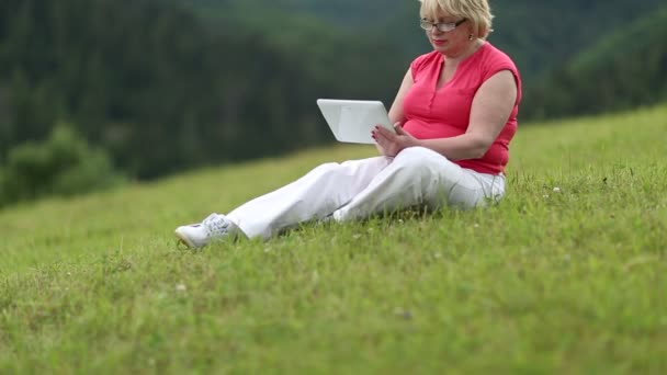 Frau sitzt auf Gras und nutzt Tablet-Computer. — Stockvideo