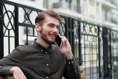 Genç yakışıklı işadamı bankta oturur ve akıllı telefonda konuşur.