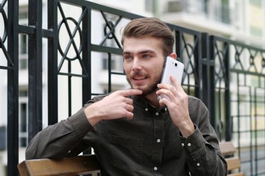 Genç yakışıklı işadamı bankta oturuyor ve cep telefonuyla konuşuyor.