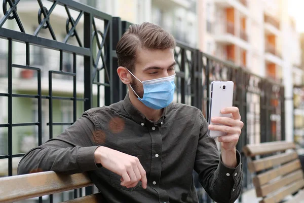 Νεαρός Άνδρας Μπλε Ιατρική Προστατευτική Μάσκα Κάθεται Στον Πάγκο Και — Φωτογραφία Αρχείου