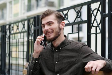 Yakışıklı iş adamı bankta oturuyor cep telefonuyla konuşuyor ve gülümsüyor.