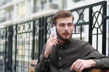 Genç işadamı bankta oturur ve akıllı telefondan konuşur.