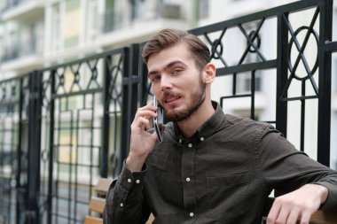 Genç adam bankta oturur ve akıllı telefonla konuşur.