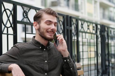 Genç ve yakışıklı iş adamı gözleri kapalı bankta oturuyor ve akıllı telefonda konuşuyor.