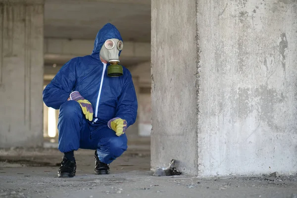 Worker in gas mask and protection suit at project site sits near body of dead bird