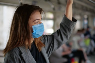 Mavi tıbbi koruyucu maskeli kadın metro vagonuna biniyor.