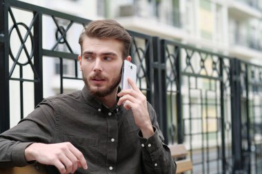 Genç işadamı bankta oturur ve akıllı telefondan konuşur.