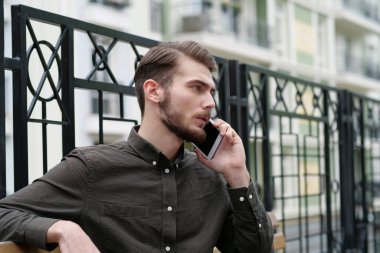 Yakışıklı iş adamı bankta oturur ve akıllı telefonda konuşur.