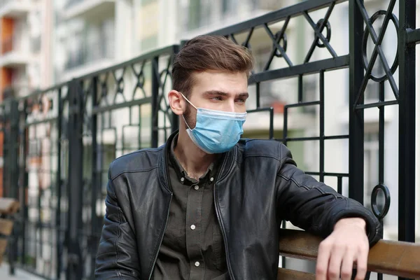 Sad depressed handsome man in medical protective face mask sits on the bench. Covid concept health and safety, coronavirus quarantine, social distancing, next wave covid virus protection
