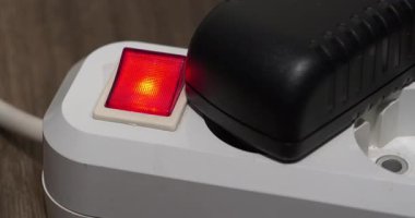 Bir adam taşınabilir bir elektrik prizinden siyah bir güç adaptörünü çıkarır ve düğmeyle elektriği keser. Güç adaptörü kırmızı güç ve gösterge ile elektrikli portatif soketi çıkartır