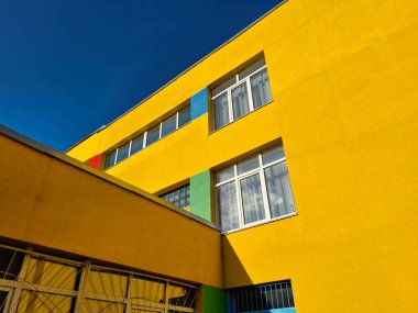 Çok renkli duvarları ve birinci katta metal parmaklıkları olan pencereleri olan okul binası cephesi.